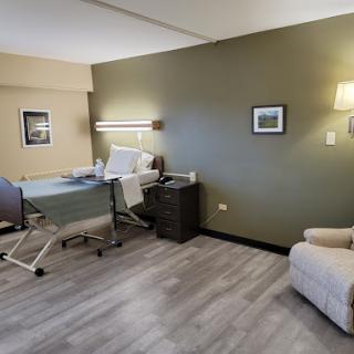 A well-lit hospital patient room featuring a bed, seating area, and minimalistic decor.