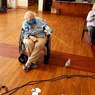 Two elderly individuals engaging in an activity at a care facility, with one using a wheelchair and wearing a mask.