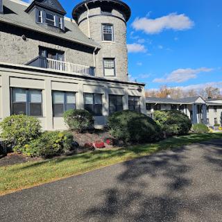 A majestic historic mansion with a tower, surrounded by a well-kept garden under a clear blue sky.