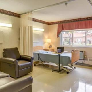 A hospital room with a bed, armchair, and window with curtains.