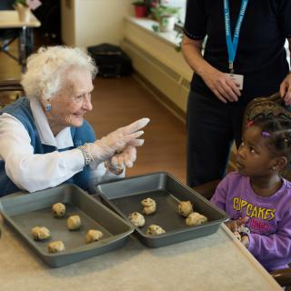 An elderly woman and a young girl enjoy baking cookies together in a kitchen setting.