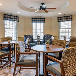 A comfortable meeting area with multiple tables and chairs, featuring large windows and a ceiling fan.