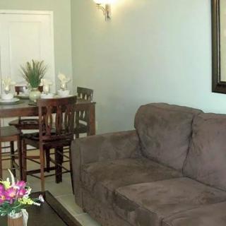 A cozy living room with a brown sofa and a dining area in the background.