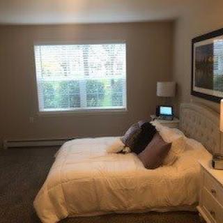 A cozy bedroom with a large window, a neatly made bed, and simple decor.