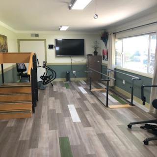 A well-equipped therapy room designed for rehabilitation exercises, featuring exercise equipment, handrails for support, and ample natural light.