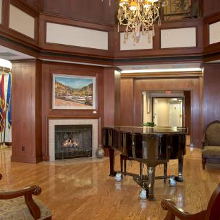 Elegant room featuring a grand piano and a cozy fireplace with wood paneling and a chandelier.