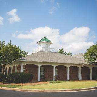 A brick building with a green-roofed cupola surrounded by trees under a blue sky.