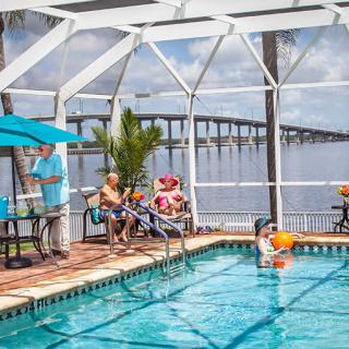 A family enjoying a sunny day by the pool with a scenic view of the bridge and water in the background.