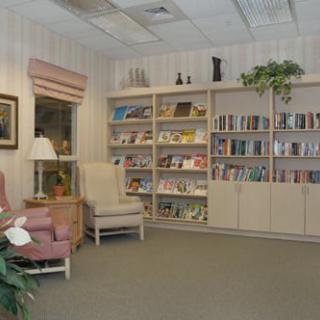 A cozy reading area in a library with bookshelves, armchairs, and a lamp.