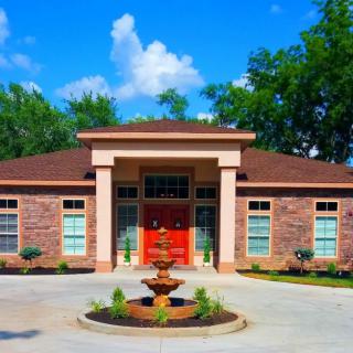 A suburban brick house with a prominent red door and a fountain in the driveway.