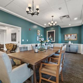 A stylish dining room with a large wooden table, surrounded by chairs, and decorated with flowers and artwork on blue walls.