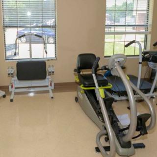 A gym room with various exercise equipment and natural light from windows.