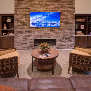 A modern living room with a brick accent wall, featuring a mounted TV, fireplace, and comfortable seating.