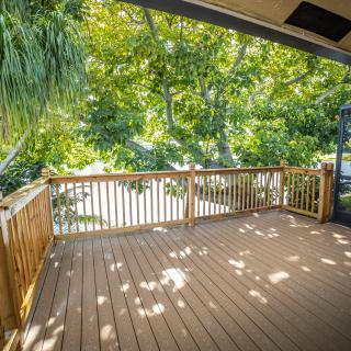A sunlit outdoor deck with wooden railings, surrounded by lush trees.