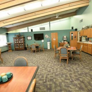 A spacious community room featuring several tables and chairs, a television, and cabinetry.