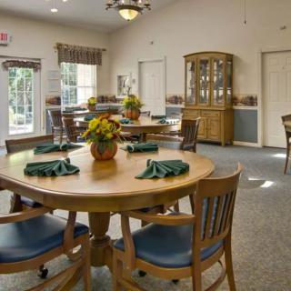 A cozy dining room with wooden tables and chairs, adorned with floral centerpieces and natural lighting.