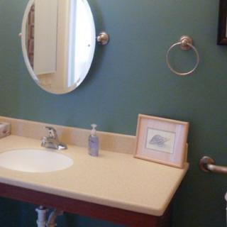 A bathroom with a green wall, featuring a sink, round mirror, soap dispenser, towel ring, and a framed picture.