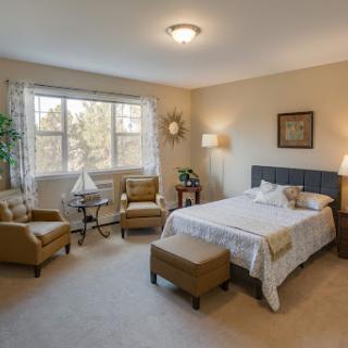 A cozy and elegantly decorated bedroom featuring a comfortable bed, two armchairs, and natural light streaming through the window.