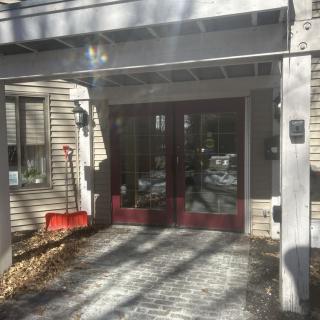 Entrance of a building with glass doors and a red shovel beside the pathway.