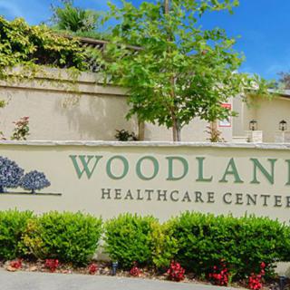 Entrance sign for Woodland Healthcare Center with surrounding greenery.