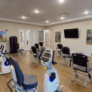 A spacious exercise room with various gym equipment and chairs arranged around a central area.