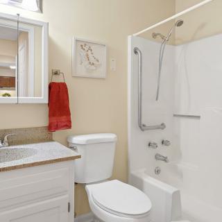 A clean and modern bathroom with a white toilet, sink, and shower equipped with a grab bar, accompanied by a red towel hanging on the wall.