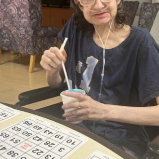 A person sitting indoors, holding a cup with a straw and engaging in a bingo game.