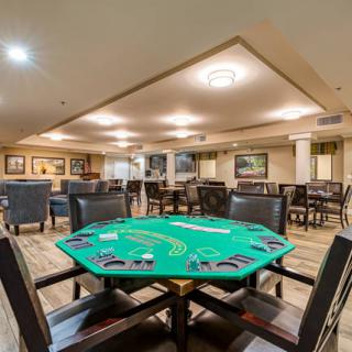 A casino gaming room featuring a poker table with green felt and surrounding seating.