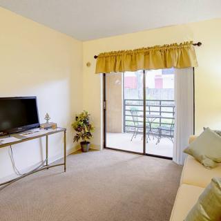 A cozy living room with a television, sliding glass door leading to a balcony, and simple decor.