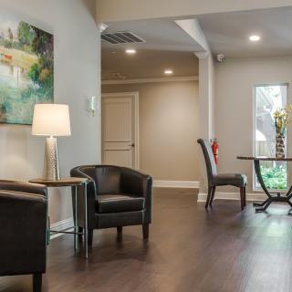 A modern lobby area featuring comfortable armchairs, a lamp, and decorative artwork.