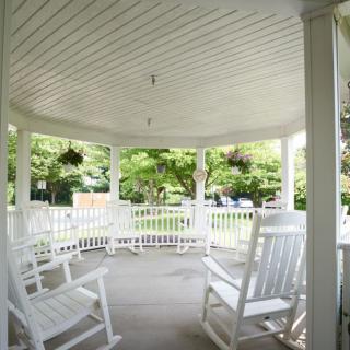 A peaceful gazebo with white rocking chairs overlooking a lush garden.