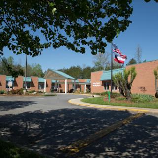 A view of a brick building with a flag, surrounded by greenery on a sunny day.