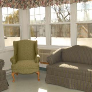 A cozy living room with an armchair and a sofa bathed in sunlight from large windows.