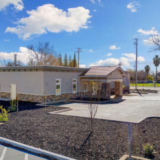 A small building with a parking lot and minimal landscaping under a clear, sunny sky.