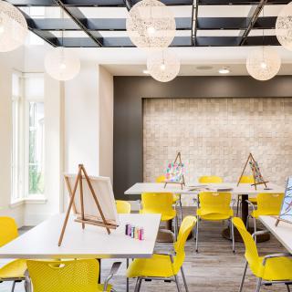 A modern art studio with yellow chairs and easels, featuring stylish lighting.