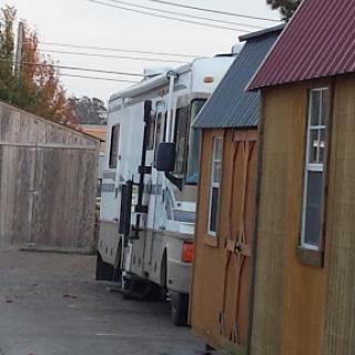 An RV parked in an alleyway between wooden storage sheds.