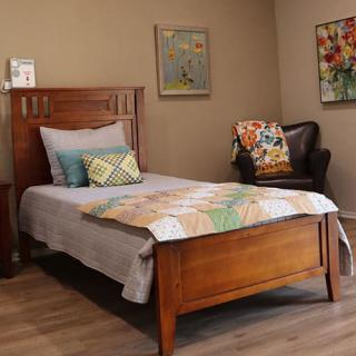 A cozy bedroom with a single wooden bed, colorful quilt, and decorative pillows, accompanied by an armchair and wall artwork.