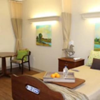 A well-furnished hospital room with a comfortable bed, paintings on the walls, and a table with chairs.