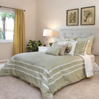 A cozy bedroom with green and white bedding, soft lighting, and decorative elements like plants and framed artwork.