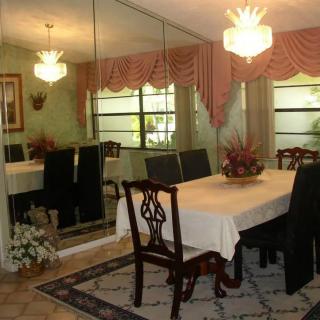 A classic dining room with a table set for six, featuring ornate chairs and a chandelier, mirrored wall panels, and elegant window drapery.