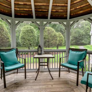 A cozy gazebo with comfortable seating and a small table, surrounded by lush greenery.