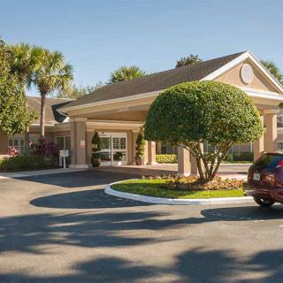 A building entrance with a driveway, landscaped trees, and a parked car.