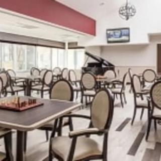A modern dining room with empty chairs and tables, featuring a chess board and a piano.