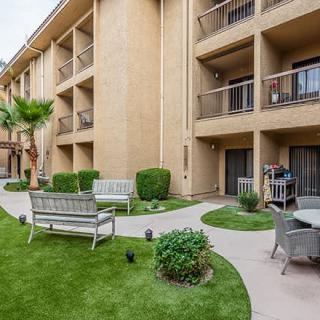 A well-maintained apartment building with outdoor seating areas, lush green lawns, and neatly landscaped pathways.