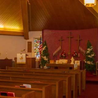 Interior of a church with decorated altar and pews, featuring crosses and Christmas trees.