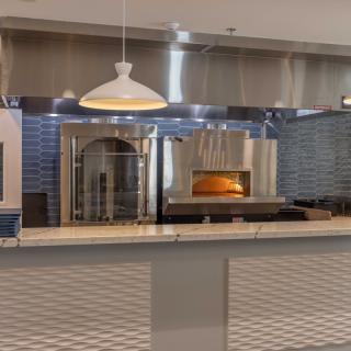 A modern restaurant kitchen featuring a wood-fired pizza oven and a tiled counter.