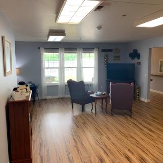 A cozy living room with wooden floors, featuring two chairs, a small table, and a television by a large window.