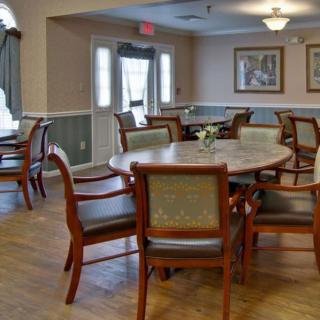 A spacious dining room with wooden tables and chairs, decorated with paintings and lit by a ceiling light.