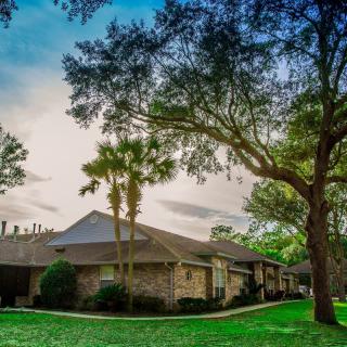 A suburban house surrounded by trees and grass under a cloudy sky.