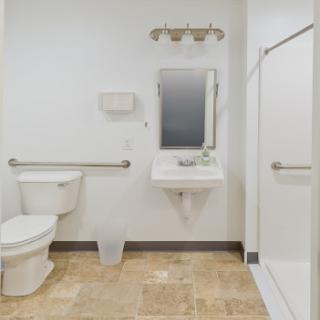 A clean and accessible bathroom featuring a toilet, sink, mirror, and shower.